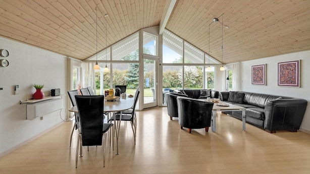 Un vaste espace de vie doté d’un haut plafond, d’une table à manger avec des chaises, d’un canapé en cuir noir et de grandes fenêtres offrant une vue sur l’extérieur.