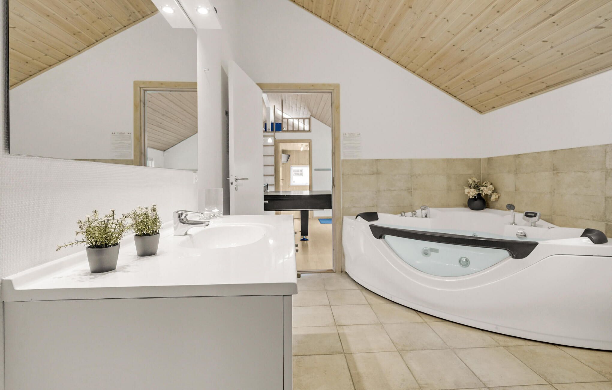 A modern bathroom with a white sink, two potted plants, a large bathtub, and a wooden ceiling.