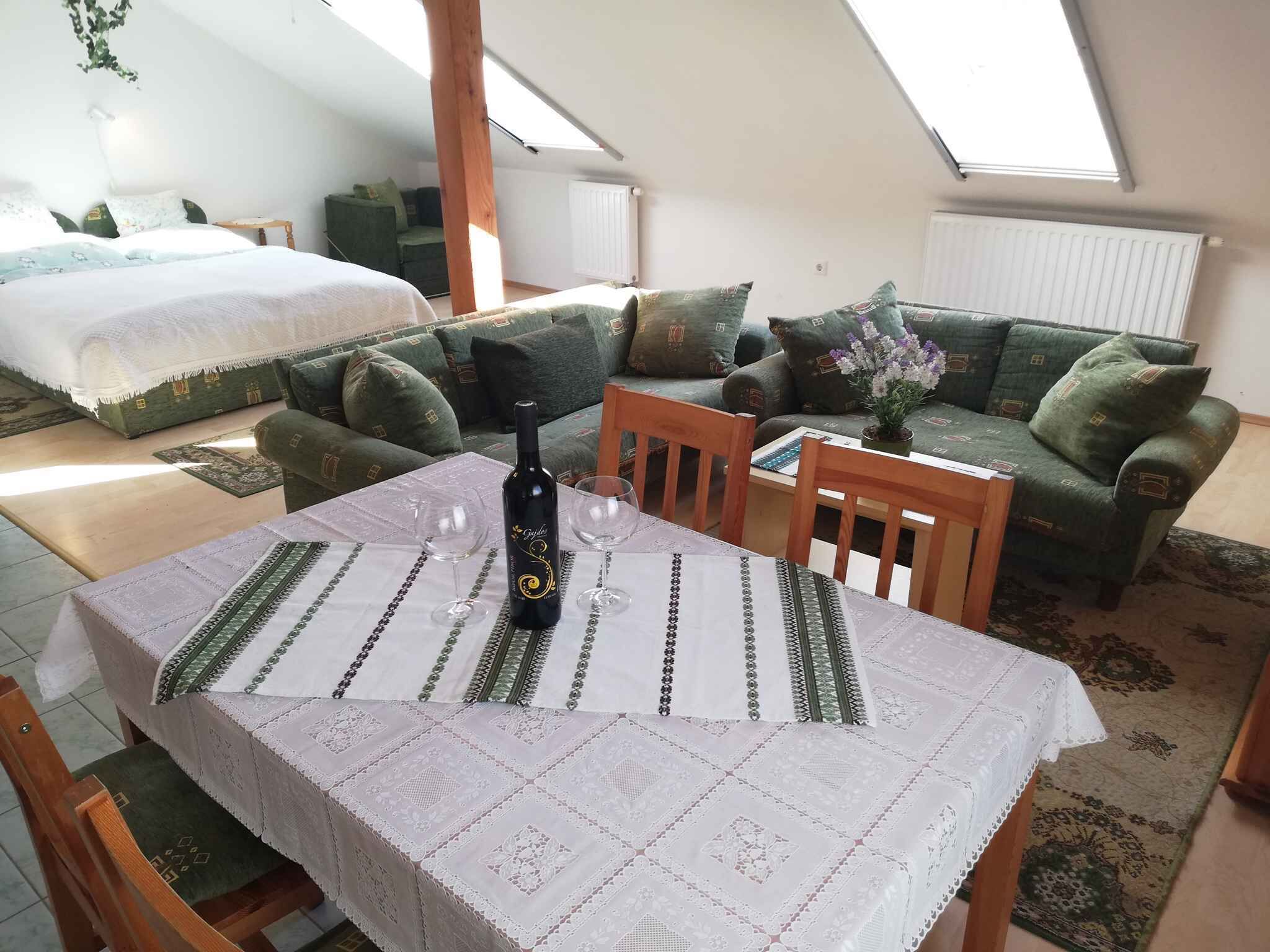 A cozy room with a bed, a green sofa, a dining table with a bottle of wine, and a view of the sky through a skylight.