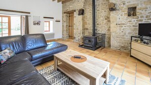 A cozy living room with a stone wall, a black leather sofa, a wooden coffee table, and a black wood-burning stove. - Beautiful home in St. Pierre Langers (St. Pierre Langers)