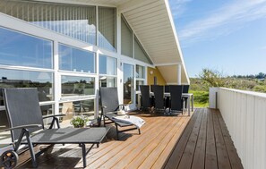 En moderne udendørs terrasse med siddepladser, store vinduer og udsigt over landskabet.