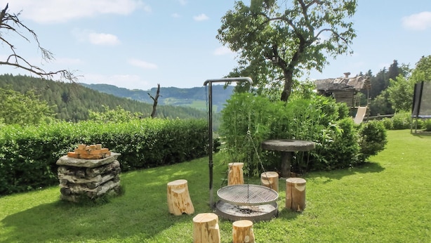 A garden with a fire pit, wooden stools, and a stone structure.