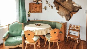 A room with a wooden dining table, two green upholstered chairs, a wooden bench, and a fur rug on the wall.