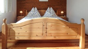 A wooden bed with a floral bedspread and two pillows, set against a wooden wall with a framed picture above.