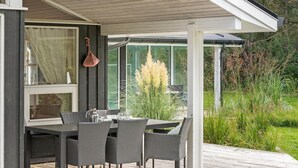 Een overdekt eethoekje buiten, met een tafel en stoelen, omringd door groen en uitzicht op de omgeving.