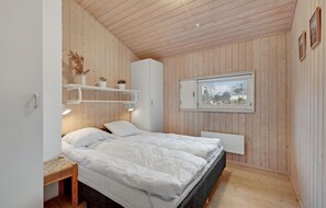 A bedroom with a wooden ceiling, a bed with white bedding, a window with a view, and a shelf with plants. - Stunning home in Knebel with sauna (Knebel)