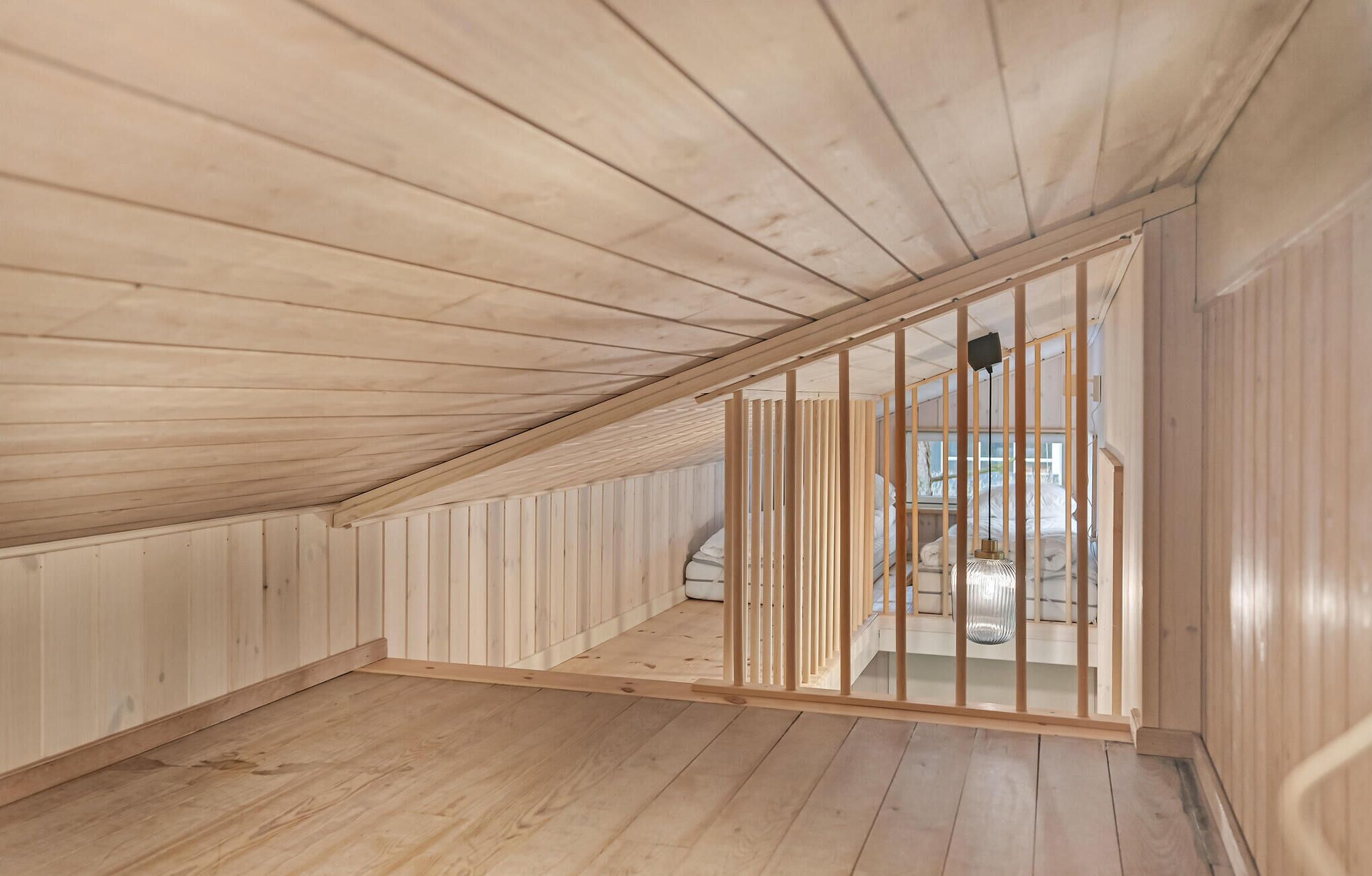 Una habitación con paredes y techo de listones de madera, una cama con ropa blanca y una lámpara colgante.