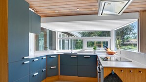 Een moderne keuken met een groot raam, inbouwmeubels en een zwarte ovenhandschoen aan de deur.