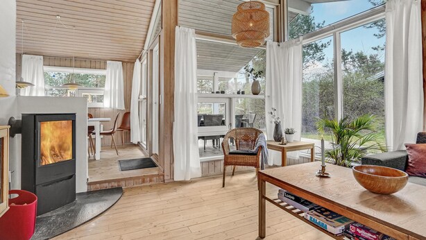 Een modern interieur met een houtkachel, een open leefruimte, een eethoek en grote ramen met uitzicht op de natuur.