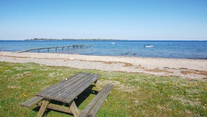 Ett picknickbord av trä står på en stenstrand, och en träbrygga sträcker sig ut i vattnet.
