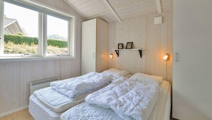 Ett rum med två sängar, ett fönster med utsikt över grönområden, en hylla med bilder och en väggmonterad lampa.