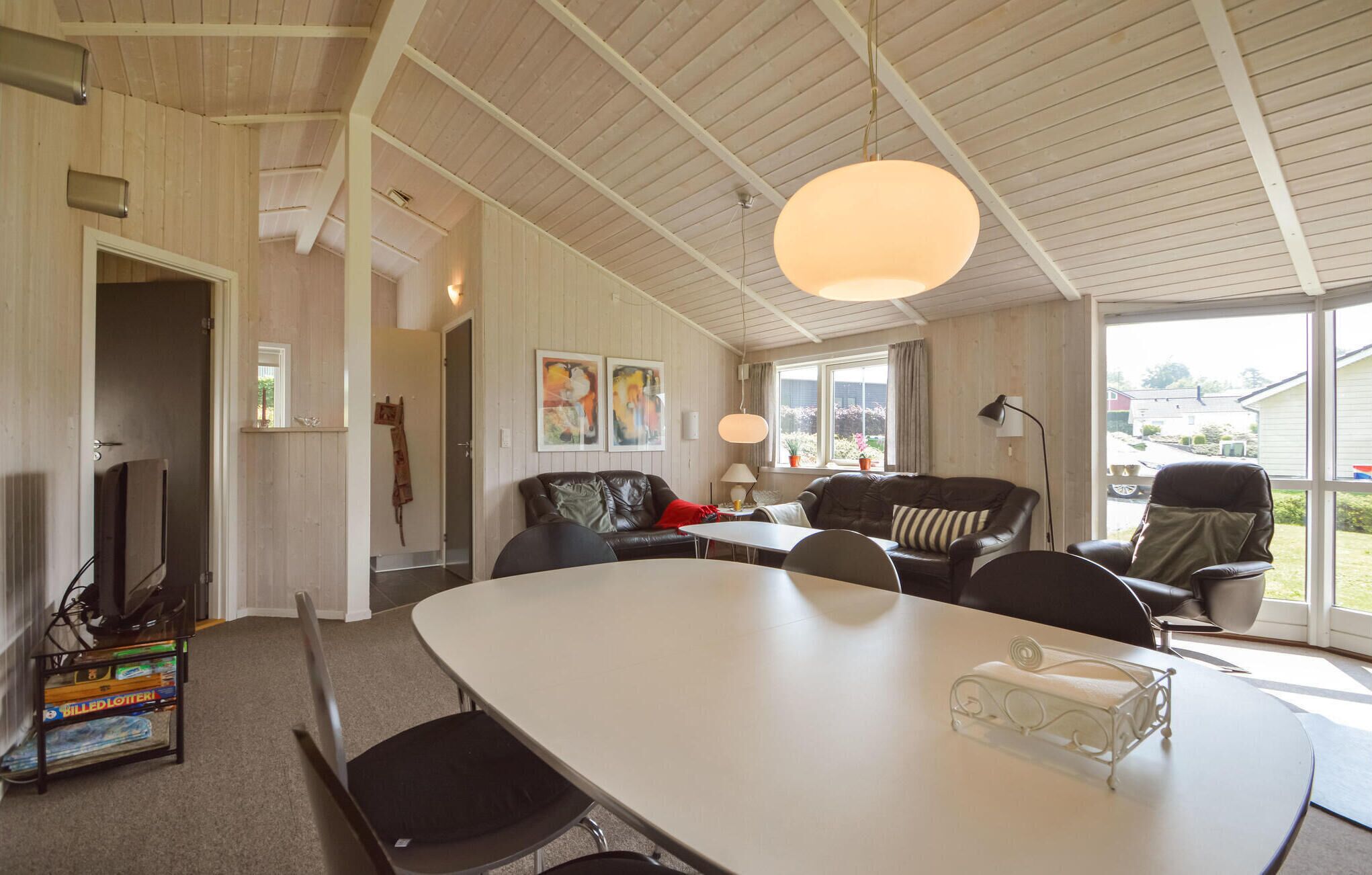 A spacious living room with a large white table, leather sofas, and a TV.