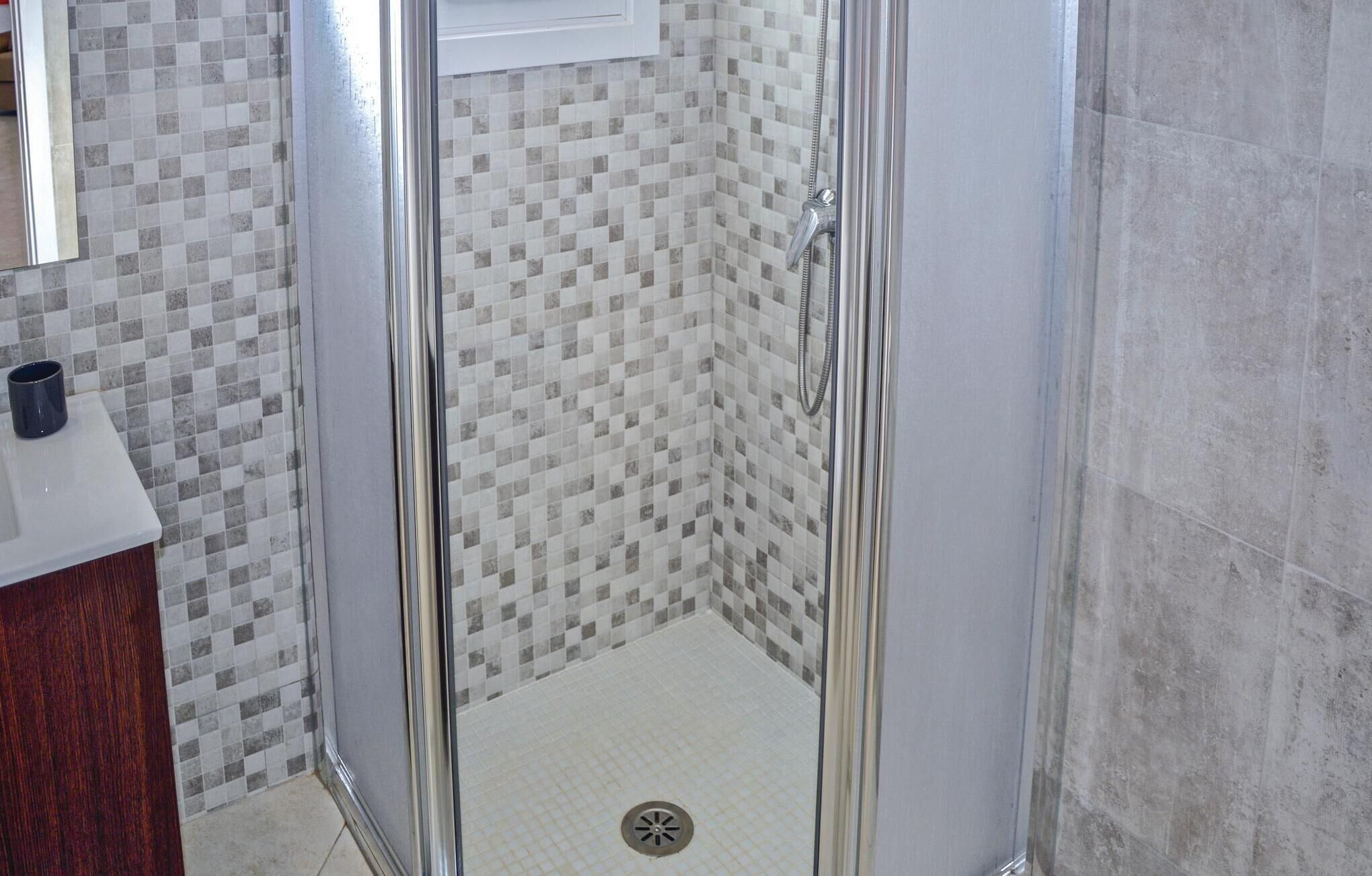 Un baño con zona de ducha, paredes con azulejos y un lavabo con una taza en la encimera.