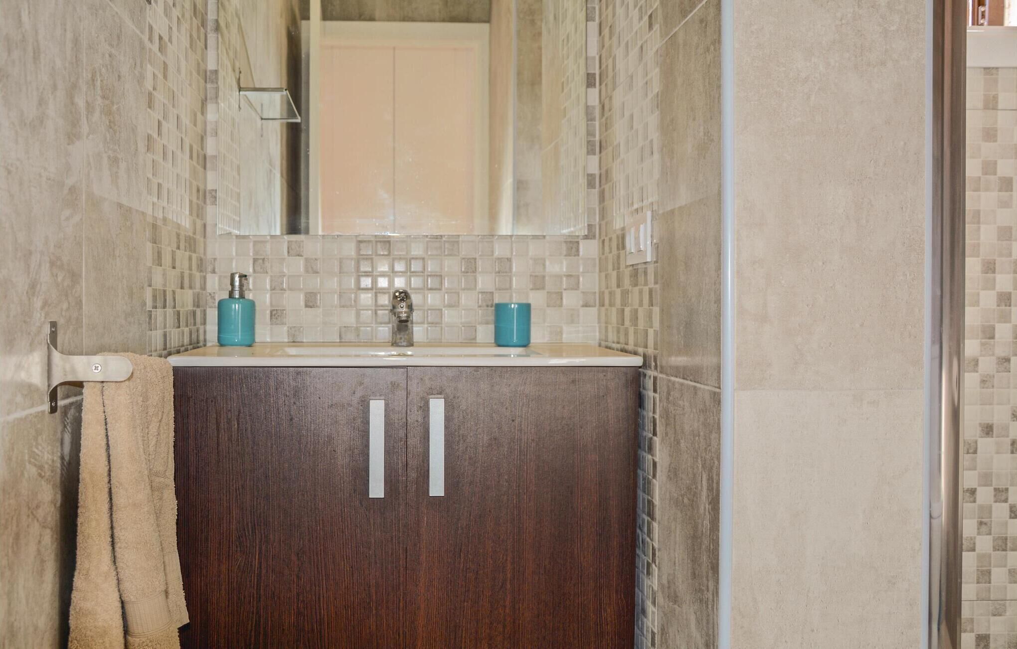 Un baño con salpicadero de azulejos, un lavabo con dos botellas azules y una toalla colgada en un perchero.