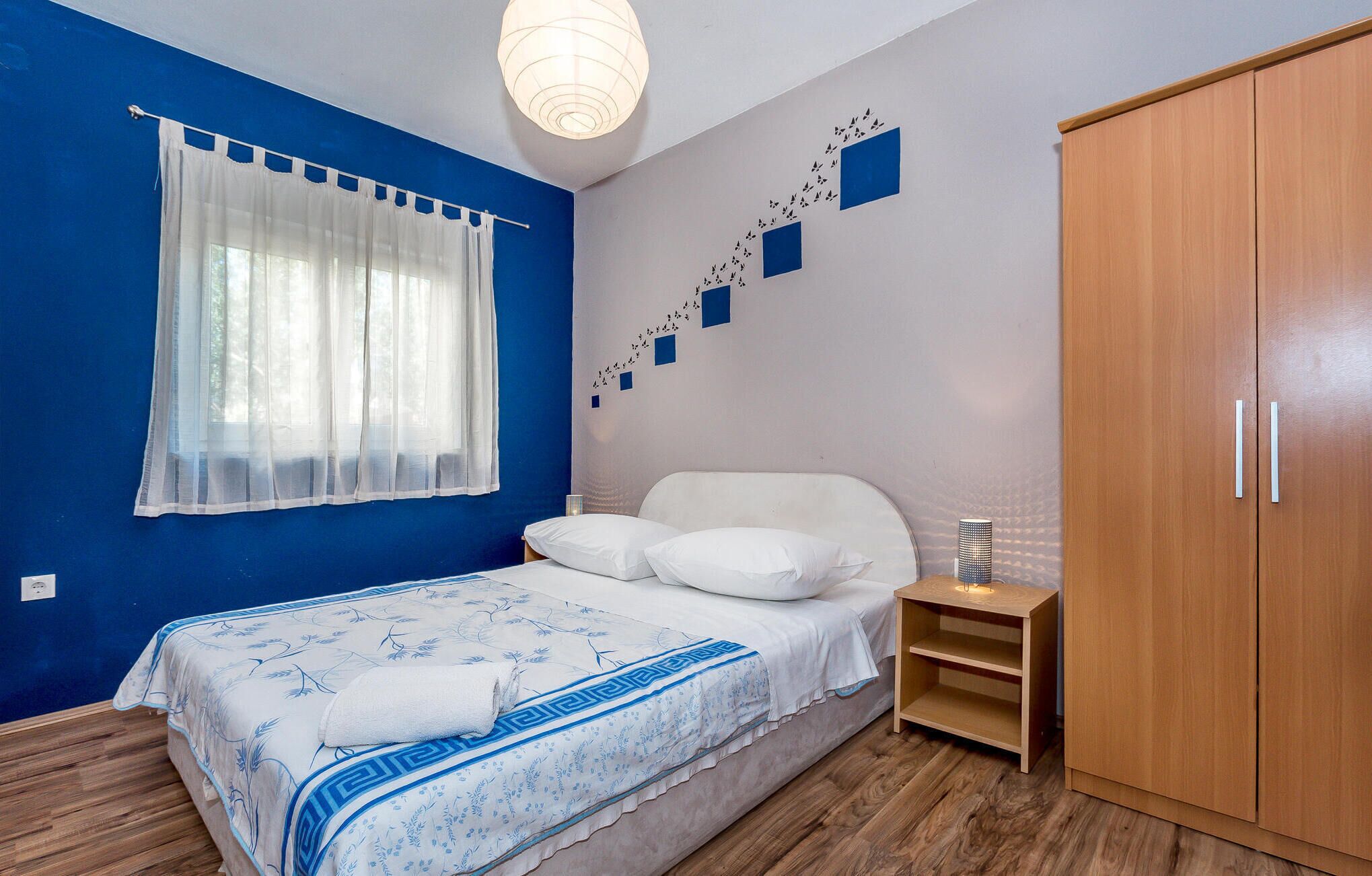 A bedroom with a bed, a wardrobe, a nightstand, and a wall with a bird mural.