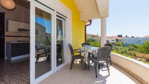 Un balcon avec une table et des chaises, une porte-fenêtre coulissante donnant sur la cuisine et une vue sur le quartier.