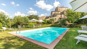 A swimming pool with lounge chairs and umbrellas, surrounded by greenery and a stone building in the background. - Cozy home in Todi PG with WiFi (Todi PG)