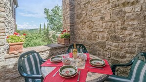 A stone-walled outdoor dining area with a table set for two, surrounded by potted plants and overlooking a scenic landscape. - Cozy home in Todi PG with WiFi (Todi PG)