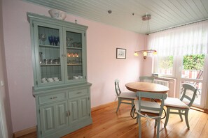 A dining area with a wooden table and chairs, a light blue cabinet with glass doors, and a window with curtains. - Vacation apartment Sonnensuite (Wustrow)