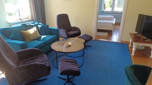 A living room with a blue sofa, two armchairs, a coffee table, and a TV stand. - Vacation apartment Sonnensuite (Wustrow)