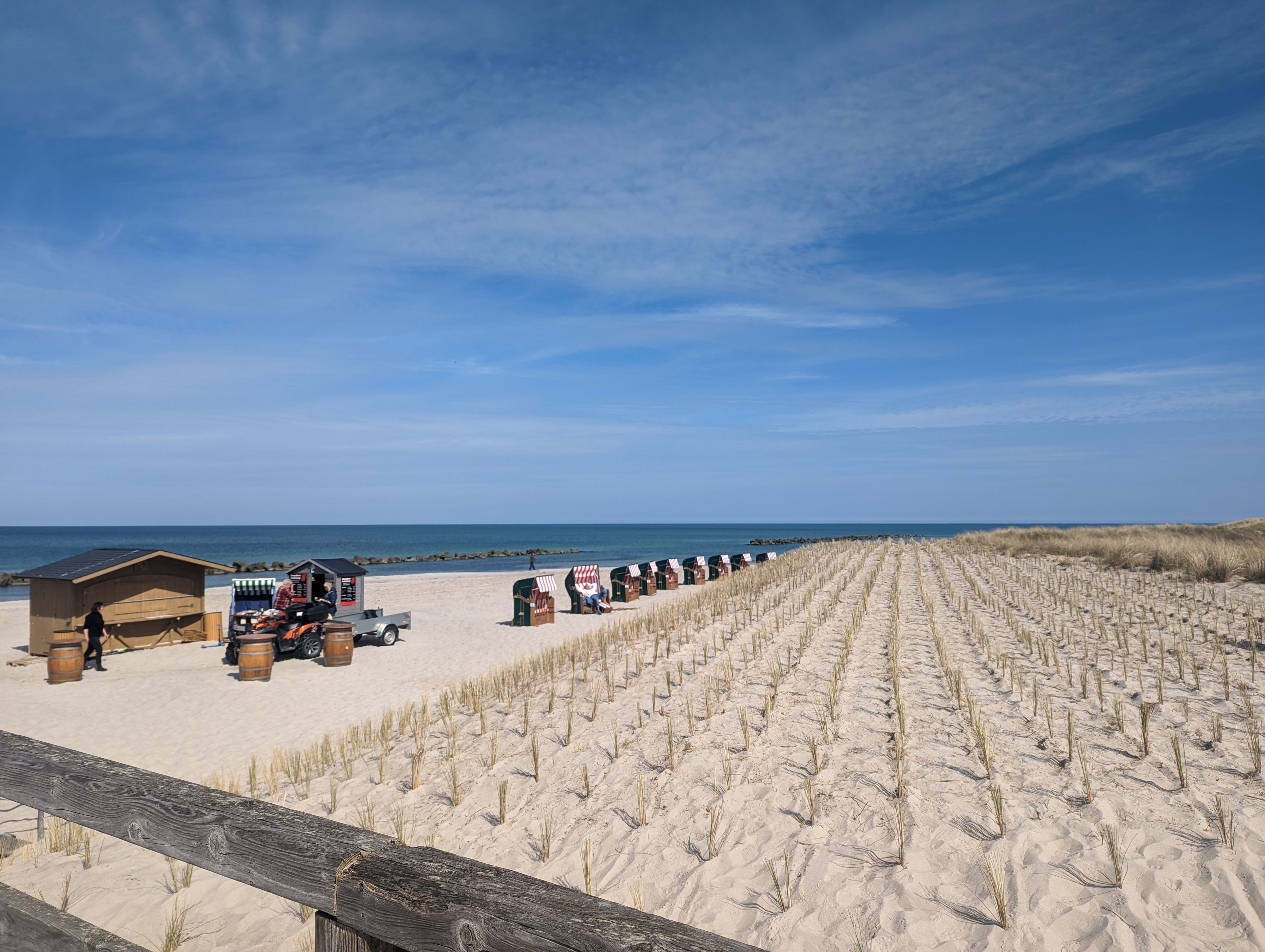 A beach with sand dunes, a wooden fence, and beach huts.