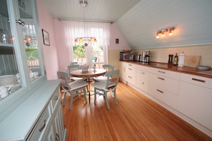 A kitchen with wooden flooring, white cabinets, a dining table with chairs, and a window with curtains. - Vacation apartment Sonnensuite (Wustrow)