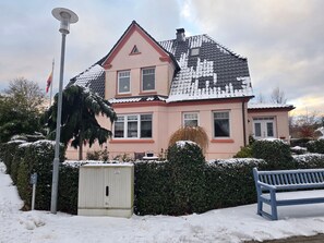 A two-story house with a snow-covered roof, a small shed, and a bench in the foreground. - Vacation apartment Sonnensuite (Wustrow)