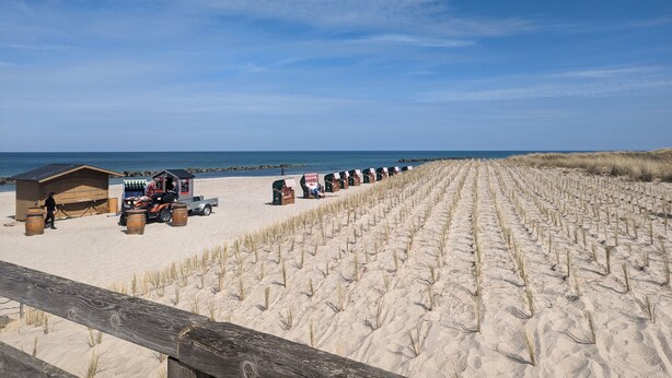 Une plage avec des dunes de sable, une clôture en bois et des cabanes de plage.