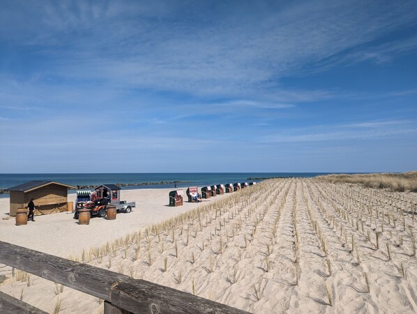 Ein Strand mit Dünen, einem Holzzaun und Strandkörben.