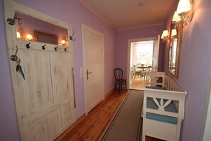 A hallway with wooden flooring, a white door, a chair, and a mirror with wall-mounted lights.