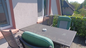 A balcony with a table and chairs, a window, and a view of a house and greenery. - Vacation apartment Sonnensuite (Wustrow)