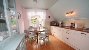 Une cuisine avec un plancher en bois, des armoires blanches, une table à manger avec des chaises et une fenêtre avec des rideaux.