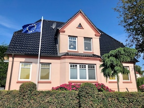 Ein zweistöckiges Haus mit einem geneigten Dach, einer Satellitenschüssel und einer Fahnenmast mit einer Flagge.