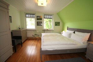 A bedroom with a bed, dresser, chair, and windows. - Vacation apartment Sonnensuite (Wustrow)