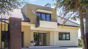 Una casa moderna de dos pisos con balcón, ventanas grandes y entrada de ladrillo.
