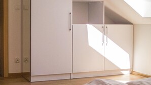 Una habitación con armario blanco, cama y techo inclinado que deja entrar luz natural.