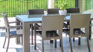 Un patio exterior con mobiliario de mimbre, incluyendo una mesa y sillas, y una planta en maceta.
