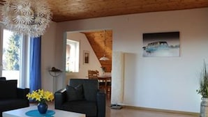A living room with a wooden ceiling, a white coffee table, a black sofa, and a painting on the wall. - Vacation apartment Schäfer (Vöhl)