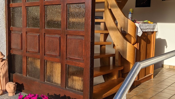 A wooden staircase with a metal handrail, a decorative door with glass panels, and a potted plant with pink flowers. - Vacation apartment Schäfer (Vöhl)