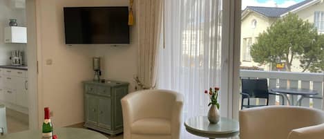 A modern living room with a flat-screen TV, a dining table with a decorative tray, a sofa, and a small round table with a vase.