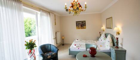 A hotel room with a bed, two chairs, a table, a chandelier, and a painting on the wall.