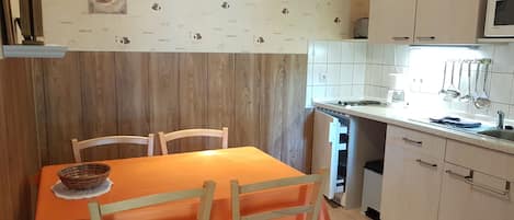 A kitchen with a wooden wall, a dining table with chairs, a microwave, and a sink.