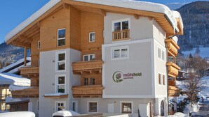 A multi-story building with wooden balconies and a snow-covered roof, surrounded by mountains.