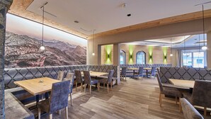 A restaurant with wooden ceiling beams, cushioned seating, and a mountain mural.