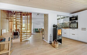 A modern kitchen with a wood-burning stove, white cabinets, and a dining area with a green sofa. - 4 bedroom lovely home in Blåvand (Blåvand)