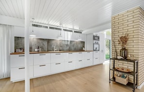 A modern kitchen with white cabinetry, a wooden countertop, and a brick accent wall. - 4 bedroom lovely home in Blåvand (Blåvand)