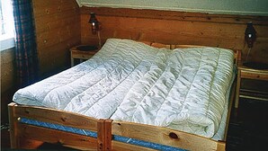 A wooden bed in a room with a sloped ceiling and two wall-mounted lamps.
