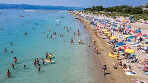 Une plage bondée, avec une eau cristalline, de nombreux parasols et des gens qui pratiquent diverses activités.