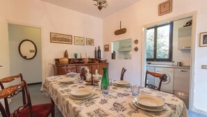 Un coin repas avec une table dressée pour quatre personnes, entourée de chaises. On y trouve également une cuisine équipée d’un lave-linge et d’une fenêtre.