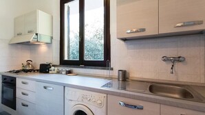 Une cuisine moderne équipée d’un lave-linge intégré, d’un évier en acier inoxydable et d’une fenêtre laissant entrer la lumière naturelle.